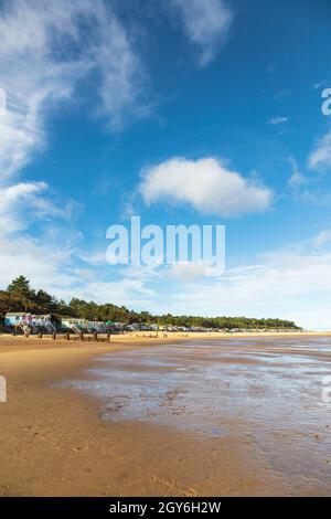 Row of Beach Huts con vista sulla baia di Holkham a Wells-Next-the-Sea sulla costa nord del Norfolk in una mattinata di ottobre luminosa e soleggiata con People Walking Foto Stock