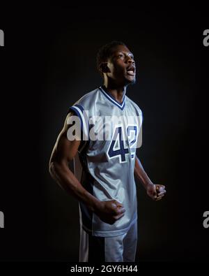 Aggressivo giocatore di basket pone in studio, sfondo nero. Baller professionista in abbigliamento sportivo, sportivo alto Foto Stock