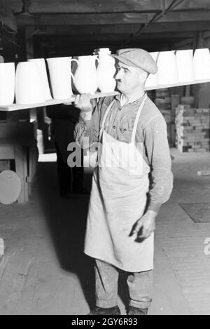 Ein Keramiker der Staatlichen Porzellanmanufaktur Berlin trägt eine tavolozza Rohkeramik mit, Deutschland 1930er Jahre. Un ceramista dello Stato manifattura di porcellana di Berlino è trascinando un pallet di materie ceramiche, Germania 1930s. Foto Stock