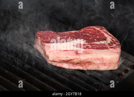 Primo piano con bistecche di manzo al ribeye per fumatori, grigliate all'aperto con griglia in ghisa e vista ad alta angolazione Foto Stock