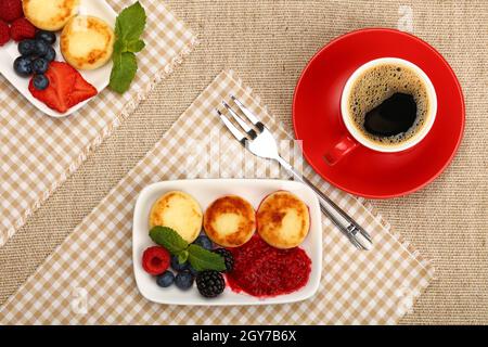 Primo piano: Porzione di dessert con frittelle al formaggio quark europeo con frutta e tazza di caffè nero, vista dall'alto, direttamente sopra Foto Stock