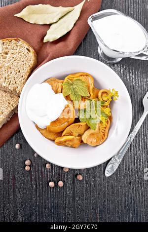 Zafferano di funghi salati con panna acida, foglia di curry e sprig di aneto in piatto, forchetta, tovagliolo e pane su sfondo nero di legno dall'alto Foto Stock