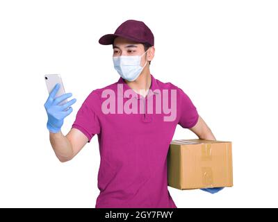 Giovane corriere che indossa abiti e cappelli rossi, indossando maschere e guanti per proteggersi, lavorando durante l'epidemia di covid-19, controllando gli smartphone t Foto Stock