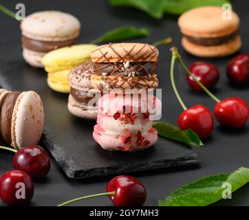 stack di macaron multicolore e ciliegie rosse mature su sfondo di legno nero, primo piano Foto Stock