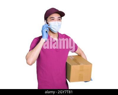 Giovane corriere che indossa abiti e cappelli rossi, indossando maschere e guanti per proteggersi, lavorando durante l'epidemia di covid-19, e parlando sul pho Foto Stock
