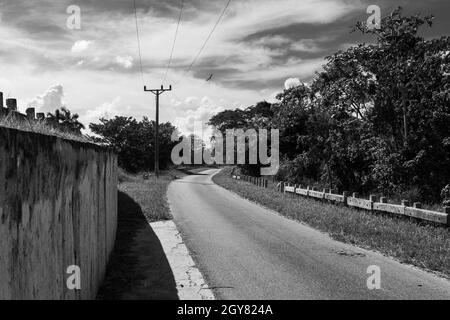 Questo è un pomeriggio caldo in una strada solitaria sul lato del counry. Il sole crea un forte contrasto con la scena. C'è una strada alpha che si forchetta, Foto Stock