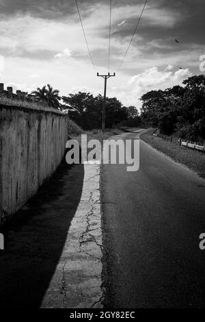 Questo è un pomeriggio caldo in una strada solitaria sul lato del counry. Il sole crea un forte contrasto con la scena. C'è una strada alpha che si forchetta, Foto Stock