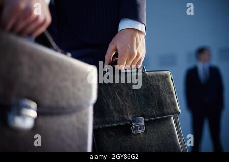 Immagine ritagliata di partner commerciali che trasportano valigette in primo piano mentre il loro collega in piedi sullo sfondo Foto Stock