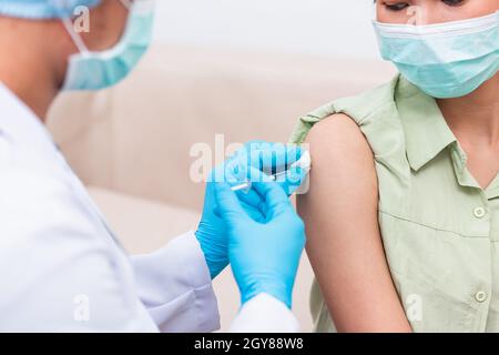 Vaccinazione, medico uomo iniezione vaccino coronavirus a giovane donna la spalla, paziente femminile in maschera medica viso, Covid-19 pandemia epidemia Med Foto Stock