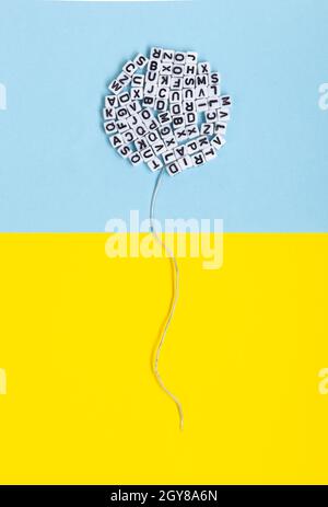 Palloncino fatto di lettere su sfondo giallo e blu. Immagine concettuale relativa alla letteratura, al linguaggio e alla libertà di espressione. Foto Stock