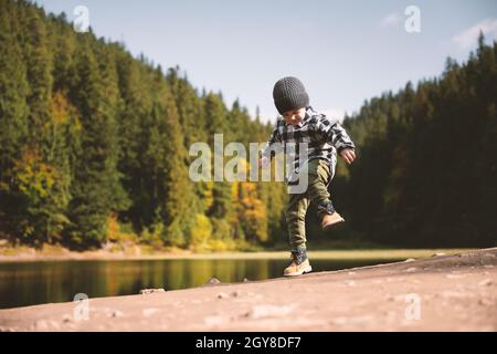 Bambino piccolo in una camicia a quadri e cappello grigio sulla costa del lago forestale. Infanzia con natura concetto di amore Foto Stock