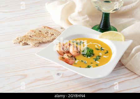 Zuppa di crema di verdure festive da zucca kuri rosso con gamberi e prezzemolo guarnire in un piatto bianco, pane e vino su un tavolo di legno chiaro per grazie Foto Stock