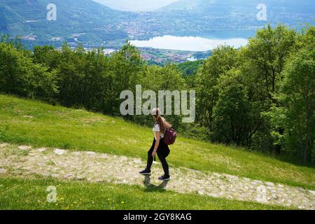 Donna escursionista cammina il sentiero e guarda con soddisfazione dalla cima della montagna il lago Foto Stock