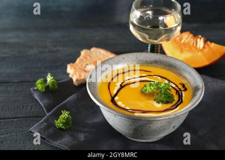 Zuppa di zucca kuri rossa con prezzemolo guarnire in una rustica ciotola blu, vino bianco e pane su un tavolo di legno scuro, pasto d'autunno per il Ringraziamento o Hallowee Foto Stock
