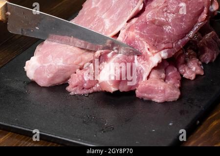 Affettare il maiale o il manzo con un coltello sul tavolo in primo piano. Preparazione di piatti a base di carne e prodotti alimentari. Pezzi di carne rossa per il kebab di shish, barbec Foto Stock