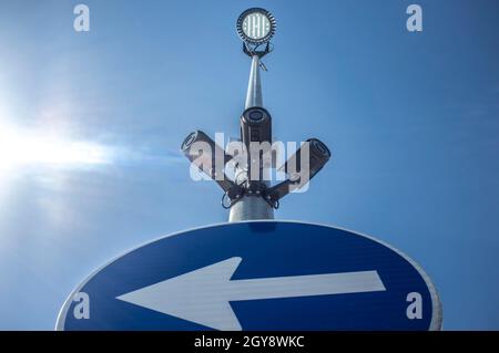 Tre telecamere di sorveglianza collegate al polo del segnale stradale con il faretto a LED sulla parte superiore. Cielo blu con raggi di sole come sfondo Foto Stock