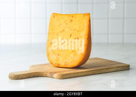 Blocco di formaggio duro con sapore di peperoncino su tagliere di legno. Foto Stock