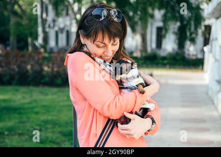 Felice giovane donna caucasica che abbraccia il suo cane piccolo, russo Toy o russo Toy Terrier, vestito in tuta d'autunno. Concetto di amore per gli animali domestici Foto Stock