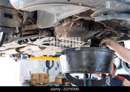 il meccanico scarica l'olio motore vecchio dalla vettura sollevata in officina Foto Stock