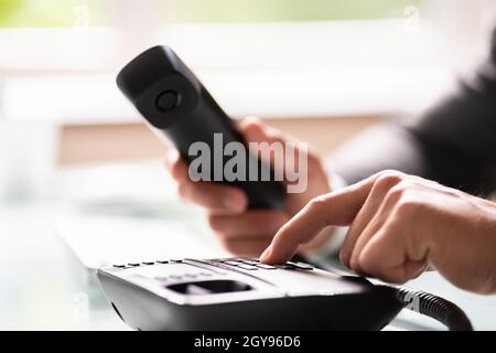 Primo piano di un uomo d'affari di composizione a mano numero di telefono da fare Chiamata telefonica in ufficio Foto Stock