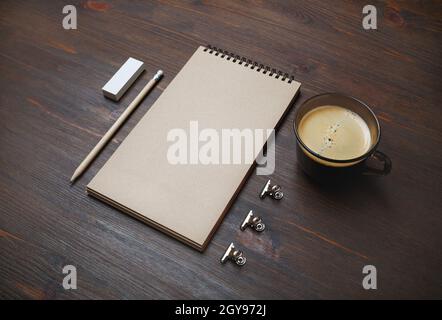 Foto di blocco note chiuso vuoto, matita, cancellatore e tazza di caffè su sfondo di tavolo in legno. Design dinamico. Elementi di cancelleria. Modello per p Foto Stock