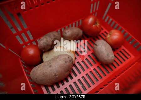 Immagine della profondità di campo poco profonda (fuoco selettivo) con patate, pomodori e pane in un cestino rosso sull'asfalto. Foto Stock