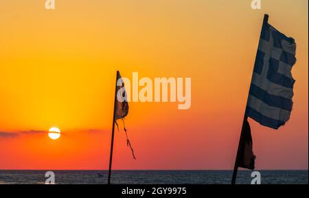 Bandiere di fronte al tramonto più bello a Ialysos Beach sull'isola di Rodi Grecia. Foto Stock