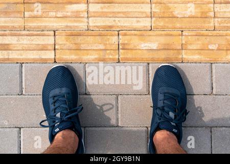 Uomo in piedi vicino alla pavimentazione tattile per handicap cieca. Pavimentazione tattile gialla per non vedenti sul marciapiede. Foto Stock