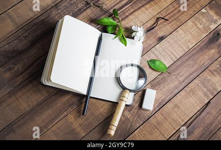 Foto di taccuino vuoto, lente d'ingrandimento, matita e gomma su sfondo tavolo in legno. Foto Stock