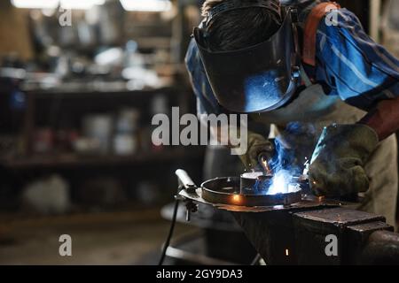 Operatore in maschera di protezione per la saldatura del metallo con attrezzatura speciale in officina Foto Stock