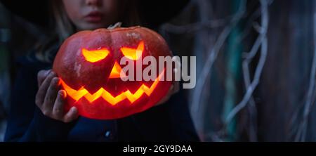 Ragazza in costume da strega, cappello con jack-o-lantern.Hand fatto di zucca grande. Candele in occhi,naso,bocca. Celebratione di halloween Holiday.Cut vicino Foto Stock