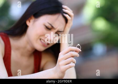 Triste donna asiatica lamentando di tenere anello di impegno per la strada Foto Stock