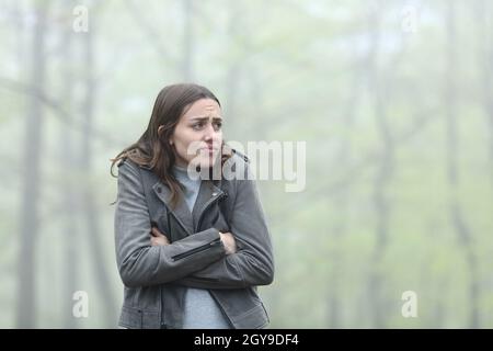 Donna stressata che fa freddo lamentandosi in un parco di nebbia Foto Stock