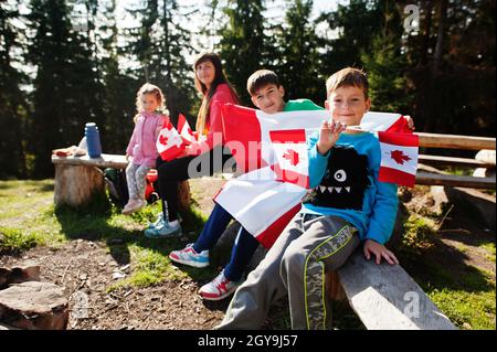 Buon giorno del Canada. Famiglia di madre con tre bambini tenere grande festa canadese bandiera in montagna. Foto Stock