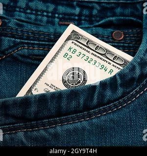 Un conto di cento dollari nella tasca dei suoi jeans. Il conto del cento dollari americani sta attanendo. Una fattura è dollari statunitensi. Stile colore.