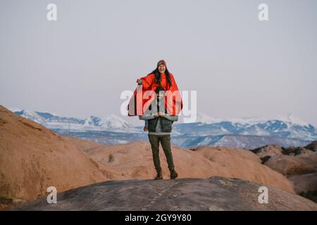 La giovane donna si siede sulle spalle dell'amico indossando il poncho in montagna Foto Stock