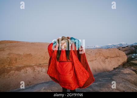 Una donna che indossa cappello e poncho puffy trekking nel deserto Foto Stock