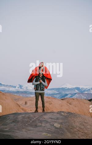 La giovane donna si siede sulle spalle dell'amico indossando il poncho in montagna Foto Stock