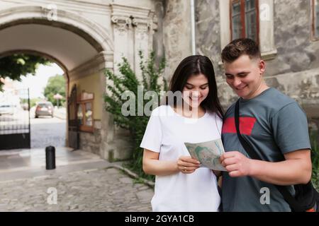 Un paio di bei turisti eterosessuali in amore guardando una mappa della città per capire come trovare un posto. La ragazza punta il dito e sorride. WIF Foto Stock