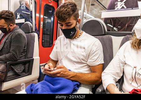 Barcellona, Spagna - 21 settembre 2021: Un giovane usa il suo cellulare mentre viaggia in metropolitana. Indossa una maschera protettiva per il viso a causa di Foto Stock