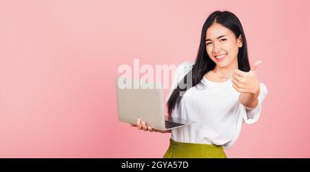 Ritratto di felice asiatico bella giovane donna sicuro sorridente faccia tenere utilizzando il computer portatile e mostrare il pollice in su per come gesto, studio shot Foto Stock