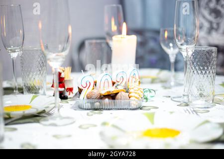 Tavolo di Natale con utensili e bicchieri, un tavolo con candele a legna, in una stanza buia Foto Stock