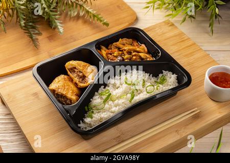 Riso con rotolo di maiale e stufato di pollo in scatola da take-out su tagliere di bambù Foto Stock