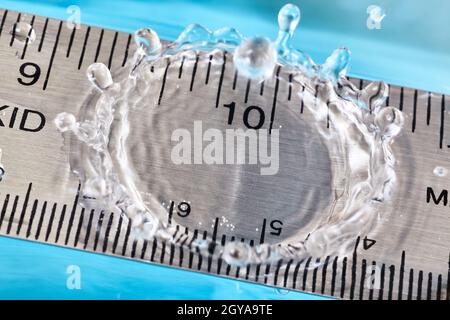 Goccia d'acqua di rimbalzo che arriva da un righello al segno di dieci-pollice Foto Stock
