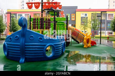 Un cortile di alti edifici con un nuovo e moderno parco giochi colorato e grande in una giornata estiva piovosa senza persone. Parco giochi all'aperto vuoto. A p Foto Stock