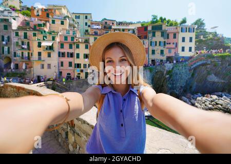 Sorridente ragazza turistica scattando foto selfie nella giornata di sole a Riomaggiore, cinque Terre, Italia Foto Stock