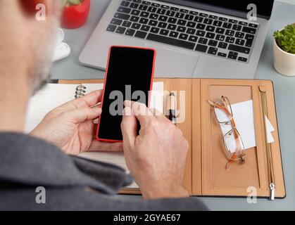Uomo che usa il telefono delle cellule e che scrive nell'ordine del giorno vicino al laptop ravvicinato in su. Concetto aziendale Foto Stock