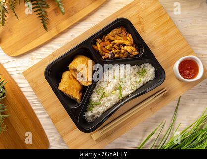 Piatto di riso con involtini di maiale e stufato di pollo servito con salsa di peperoncino dolce su tagliere di bambù Foto Stock