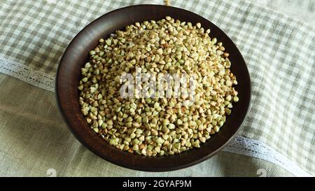 Grano saraceno crudo verde in una piastra di argilla marrone su uno sfondo marrone. Concetto di cibo biologico vegano. Il concetto di dieta, perdita di peso, nutr sano e corretto Foto Stock