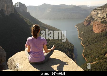 Indietro vista ritratto a corpo pieno di una donna che fa yoga lotus posa sulla cima di una scogliera Foto Stock